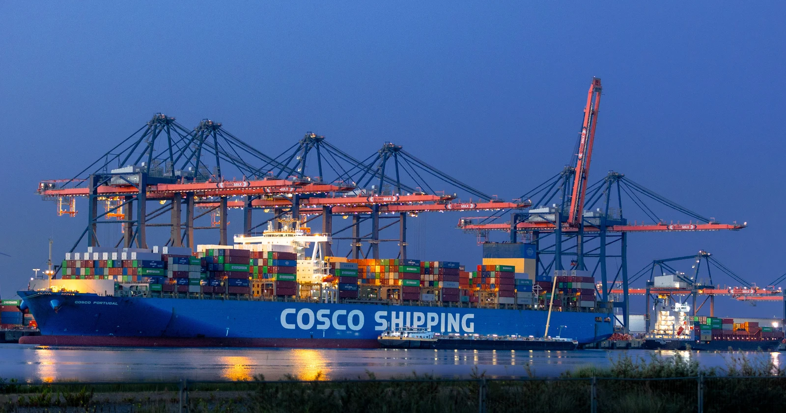 COSCO SHIPPING container ship docked beneath port cranes at dusk